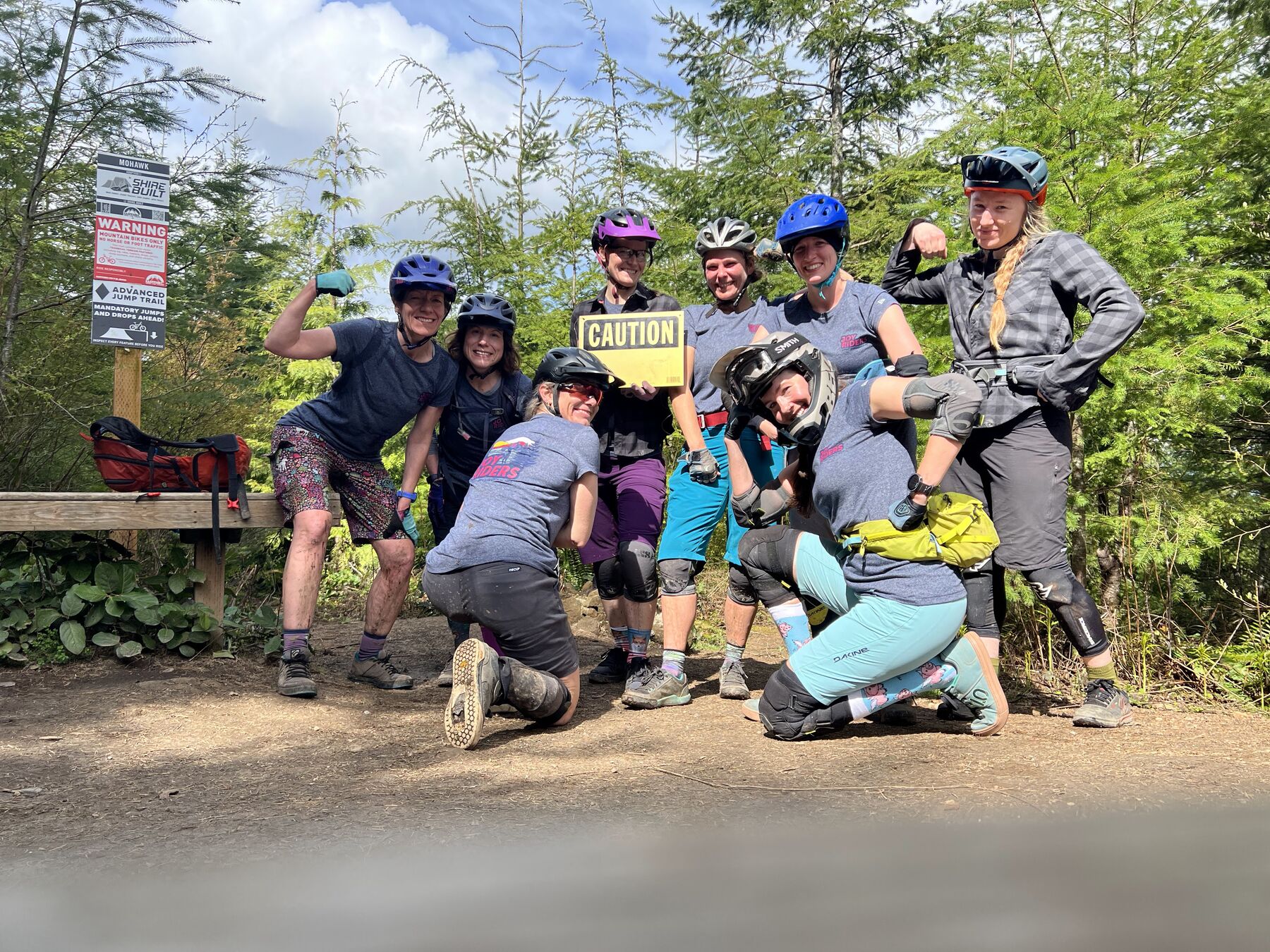 A group of JoyRiders striking poses by a trail caution sign