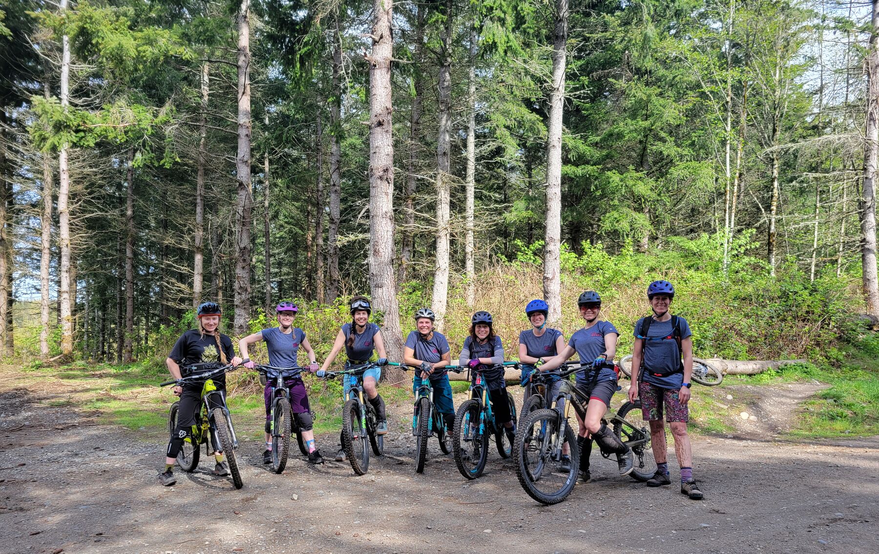 Eight JoyRiders lined up with their bikes on a forest road